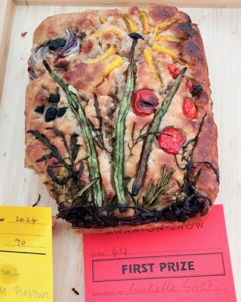 Decorated focaccia. 3 green beans as flower stalks with yellow pepper for the flower petals. A black olive cut up for an insect and red cherry tomatoes as berries